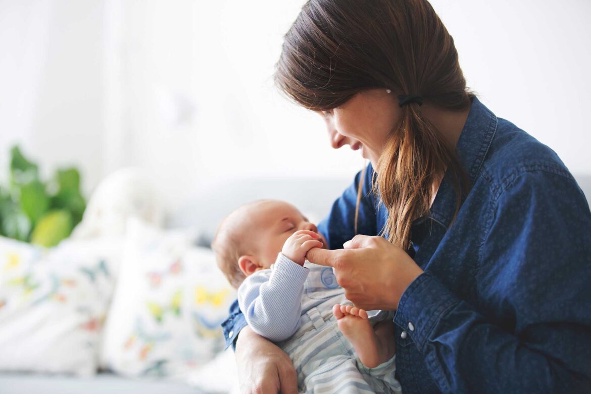 Mama trzyma niemowlę siedząc na kanapie.